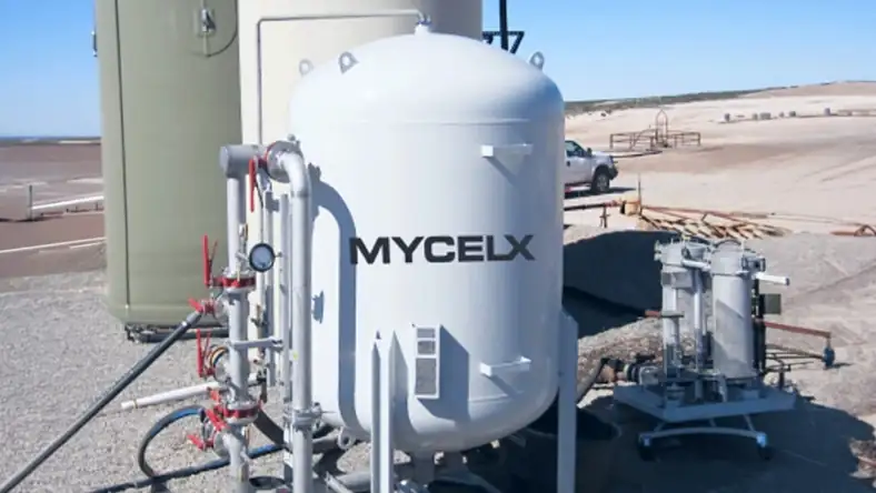 White industrial treatment tank marked with a company logo standing on a gravel pad under a clear blue sky